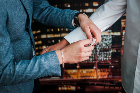 The man fastens the cufflink on the sleeve of his shirt. The groom fastens a button on the sleeve of...