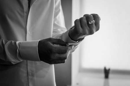 The man fastens the cufflink on the sleeve of his shirt. The groom fastens a button on the sleeve of...