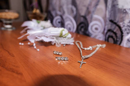 Earrings, a gold ring with a gem and a silver chain with a cross on a brown background