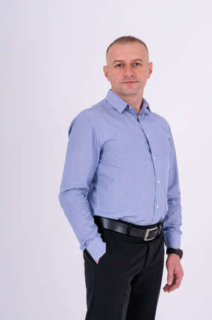 A man in a blue shirt and black trousers stands on a white backgroundの写真素材