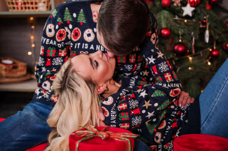 A guy with a girl in a sweater and jeans are hugging on the background of a Christmas tree and red giftsの写真素材