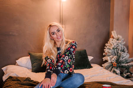 A girl in a sweater is lying on the bed. Tangerines on the bed and a red mug