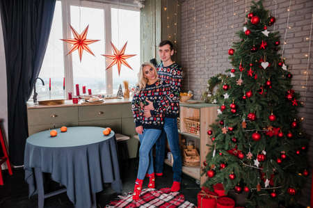 A guy with a girl in a sweater stands near the kitchen and hugs