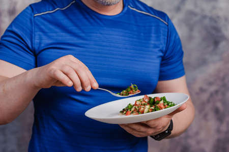 Salad with cucumber, tomato and green onions on a plate. A man holding a plate of saladの写真素材