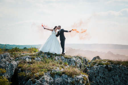 Newlyweds stand on a rock and hold colored smoke in their handsの写真素材