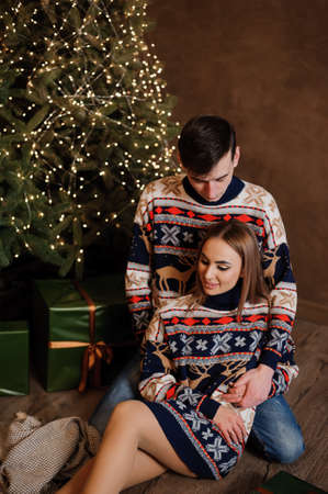 A guy and a girl hug and kiss against the background of a Christmas tree and a red sofaの写真素材