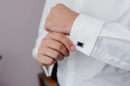 Man fastening a cuff-link on the shirt. Groom fastens cufflinks on the shirt