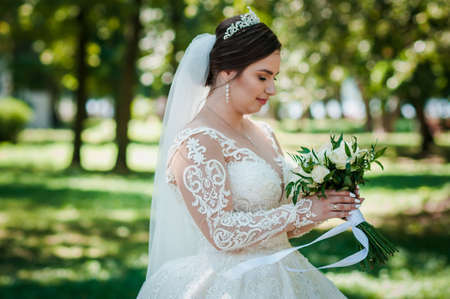 Portrait of a bride in a beautiful white dress on a green background. Bride with a bouquet of flowersの写真素材
