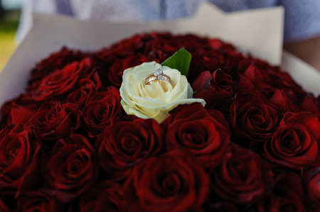 Bouquet of red roses, womens gold ring with a stone. Bouquet of red flowers. An offer of marriage