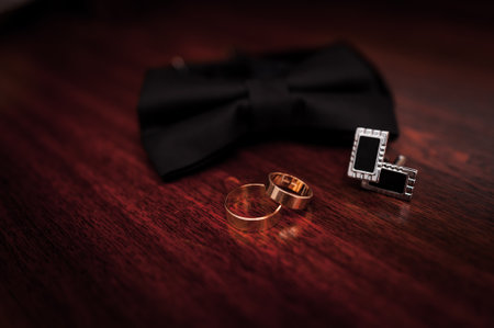 Black bow tie, wedding gold rings on brown wooden background