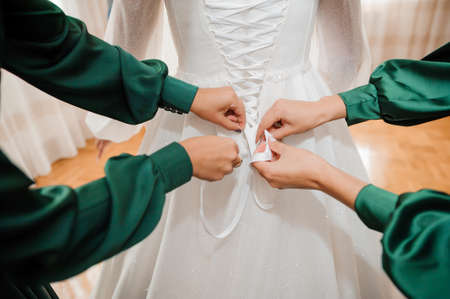 Bridesmaids tie a bow on the wedding dress. Morning of the brideの写真素材