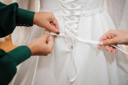 Bridesmaids tie a bow on the wedding dress. Morning of the bride