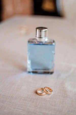 A pair of gold wedding rings, a jar of perfume on the background