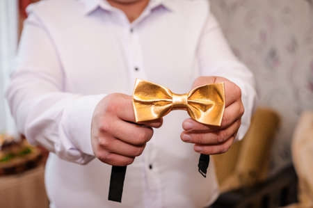 Golden bow tie in the hands of the groom. Bow tie in the hands of a manの写真素材