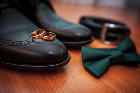 Leather black shoes, a belt, a pair of gold rings, a green butterfly tie on a backgroundの写真素材