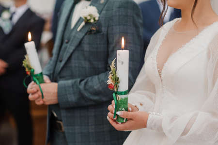 The bride and groom hold shining candles during the ceremony in the church. Hands of newlyweds with candles in the church. Church religious detailsの写真素材