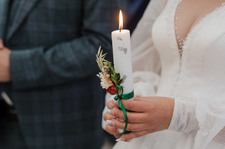 The bride and groom hold shining candles during the ceremony in the church. Hands of newlyweds with...