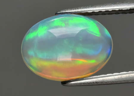 Natural gemstone opal in tongs on background