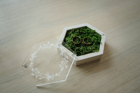 Two gold wedding rings on green moss in a white wooden box.