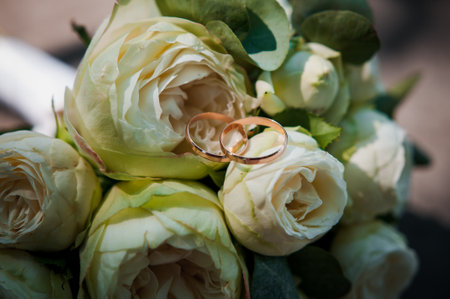 A pair of gold wedding rings on a bride's bouquet with white flowers.の写真素材