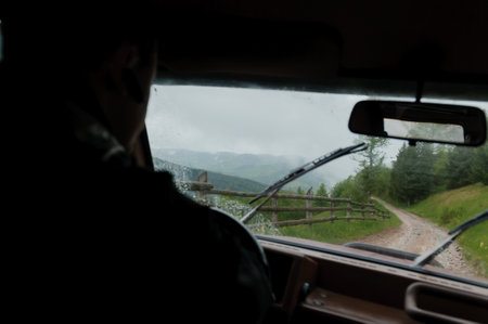 The view from the car window is a landscape of mountains, a forest against the backdrop of mountains, a road after rain. silhouette of a guy driving a carの写真素材