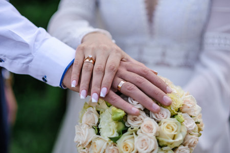Wedding rings on the hands of the newlyweds, a bouquet of flowers in the background. Gold rings on...