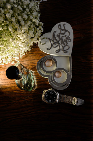 wedding accessories. Wedding invitation, a pair of gold wedding rings in a white heart-shaped wooden box, a bride's bouquet, perfume, watchの写真素材