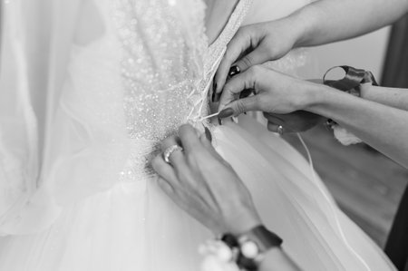 Bridesmaids tie a bow on the wedding dress. Morning of the brideの写真素材