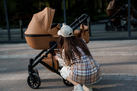 Portrait of a beautiful girl. Close-up photo of a beautiful girl in a plaid shirt and a cap. The girl stands near the brown baby carriage. Mother walking with a small childの写真素材