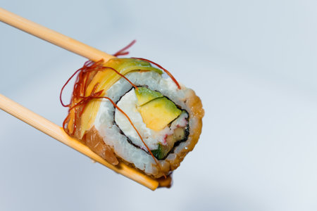 Sushi rolls with rice, avocado, red fish close-up in chopsticksの写真素材