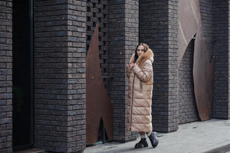 Beautiful young pregnant woman in a brown coat, in the background a brick wall.の写真素材