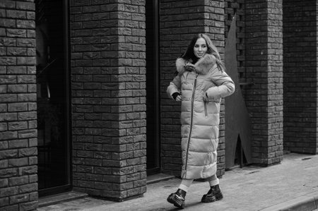 Beautiful young pregnant woman in a brown coat, in the background a brick wall.の写真素材