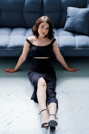 Young beautiful girl in a black dress sitting on the sofa