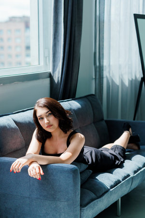 Young beautiful girl in a black dress sitting on the sofa