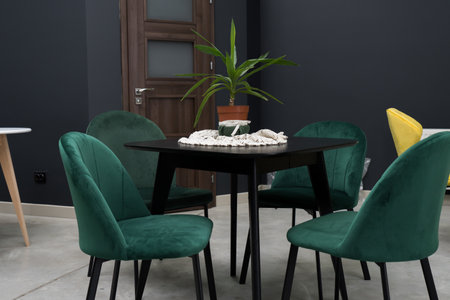 Black wooden table combined with green wooden chairs with soft fabric upholstery. There is a green...