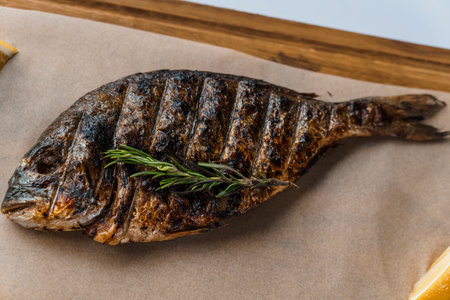 Dorado fish baked with lemon and rosemary on a barbecue on a wooden boardの写真素材