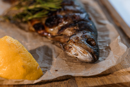 Dorado fish baked with lemon and rosemary on a barbecue on a wooden boardの写真素材