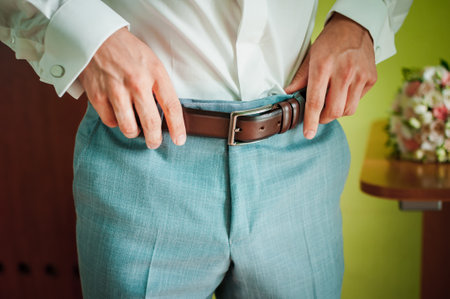 Elegant Groom Adjusting Belt on Wedding Day in Stylish Attire.の写真素材