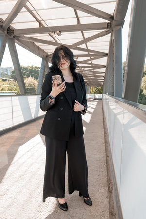 Confident Businesswoman with Smartphone Standing on Modern Urban Bridge.の写真素材