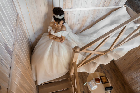 Elegant Bride in Exquisite Gown Seated on Rustic Wooden Stairs Captured in Dreamy Overhead View.の写真素材