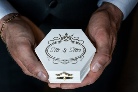 Elegant Close-Up of Hands Holding a Wedding Ring Box with Mr & Mrs Inscription