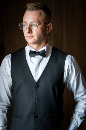 Elegant Gentleman in Formal Attire Stands Poised Against Subtle Wooden Backdrop.の写真素材