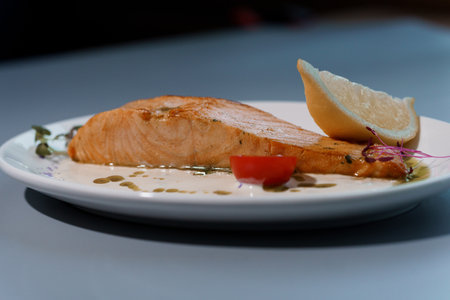 Gourmet Delight of Grilled Salmon Fillet with Lemon and Creamy Sauce on Elegant White Plate.の写真素材