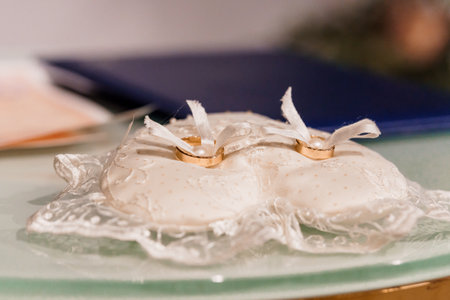 Elegant Wedding Rings on Decorative Pillow Surrounded by Soft Lighting.の写真素材