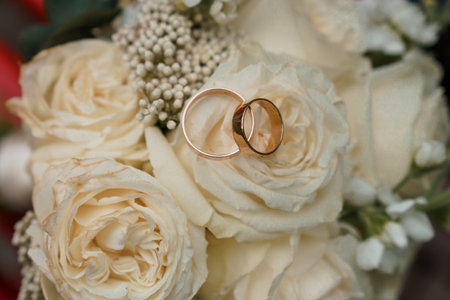 Elegant wedding rings resting on a bouquet of soft cream roses adorned with delicate baby's breath.