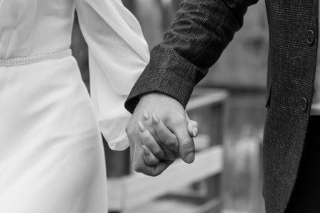 Romantic Black and White Close-Up of Intertwined Hands of a Bride and Groom in a Serene Outdoor Setting.の写真素材