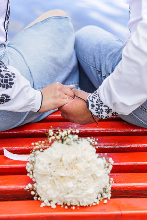 Romantic Couple Holding Hands with Floral Bouquet on Rustic Red Bench.の写真素材
