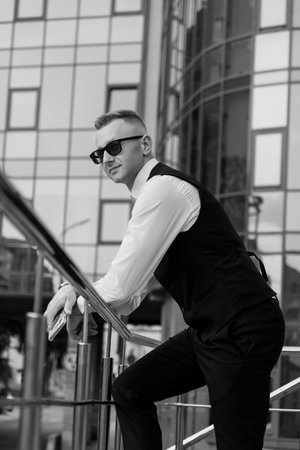 Stylish Young Man in Sunglasses Posing Against a Modern Glass Building.の写真素材