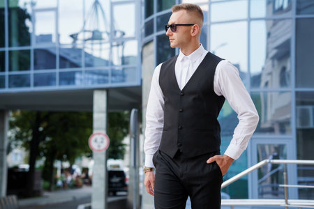 Elegant Businessman in Stylish Vest and Sunglasses Posing Outdoors.の写真素材