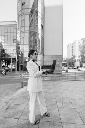 Stylish Businesswoman in Suit Working on Laptop in Urban Environment.の写真素材